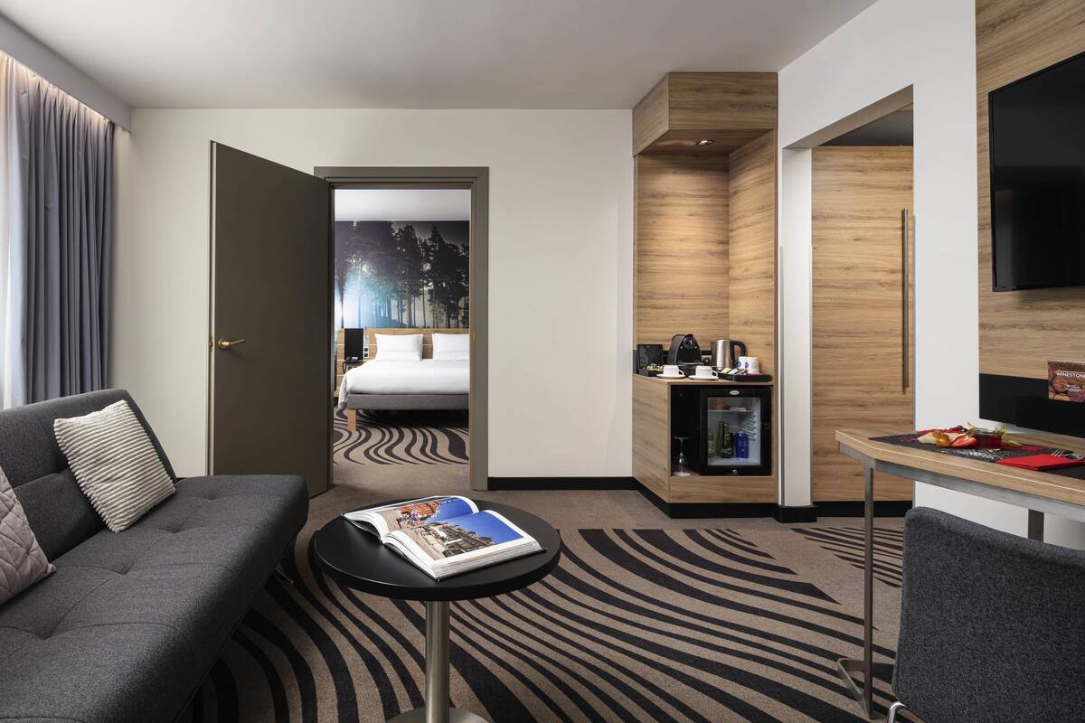 Ein modernes Hotelzimmer mit einem Bett, einer Sitzecke mit einer Zeitschrift, einer kleinen Küchenzeile und einem Fernseher.