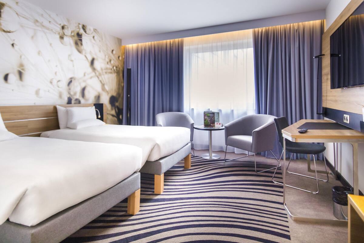 Ein modernes Hotelzimmer mit zwei Betten, einem Schreibtisch und einem Stuhl.