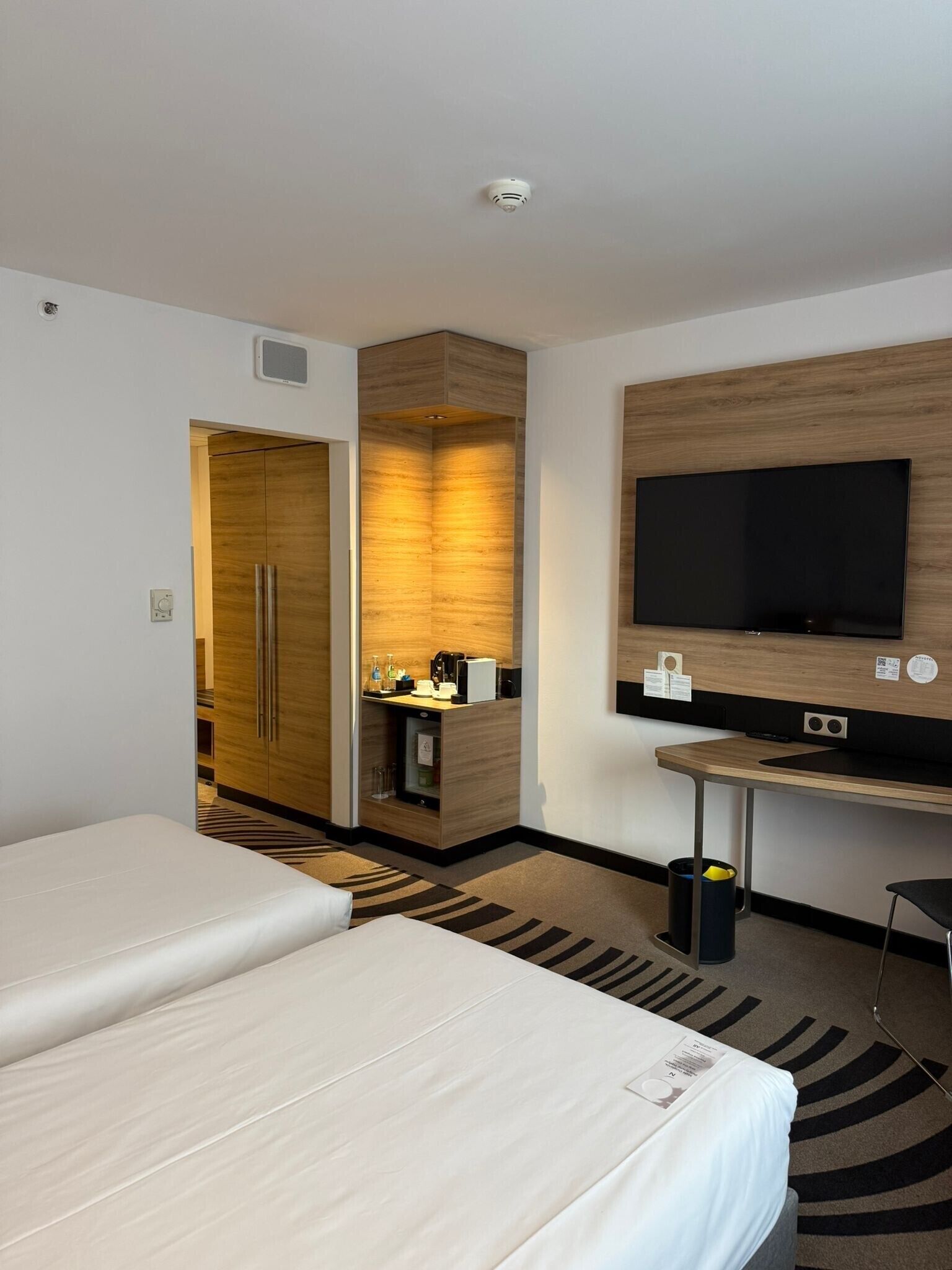 A hotel room with two beds, a TV, a desk, and a minibar.
