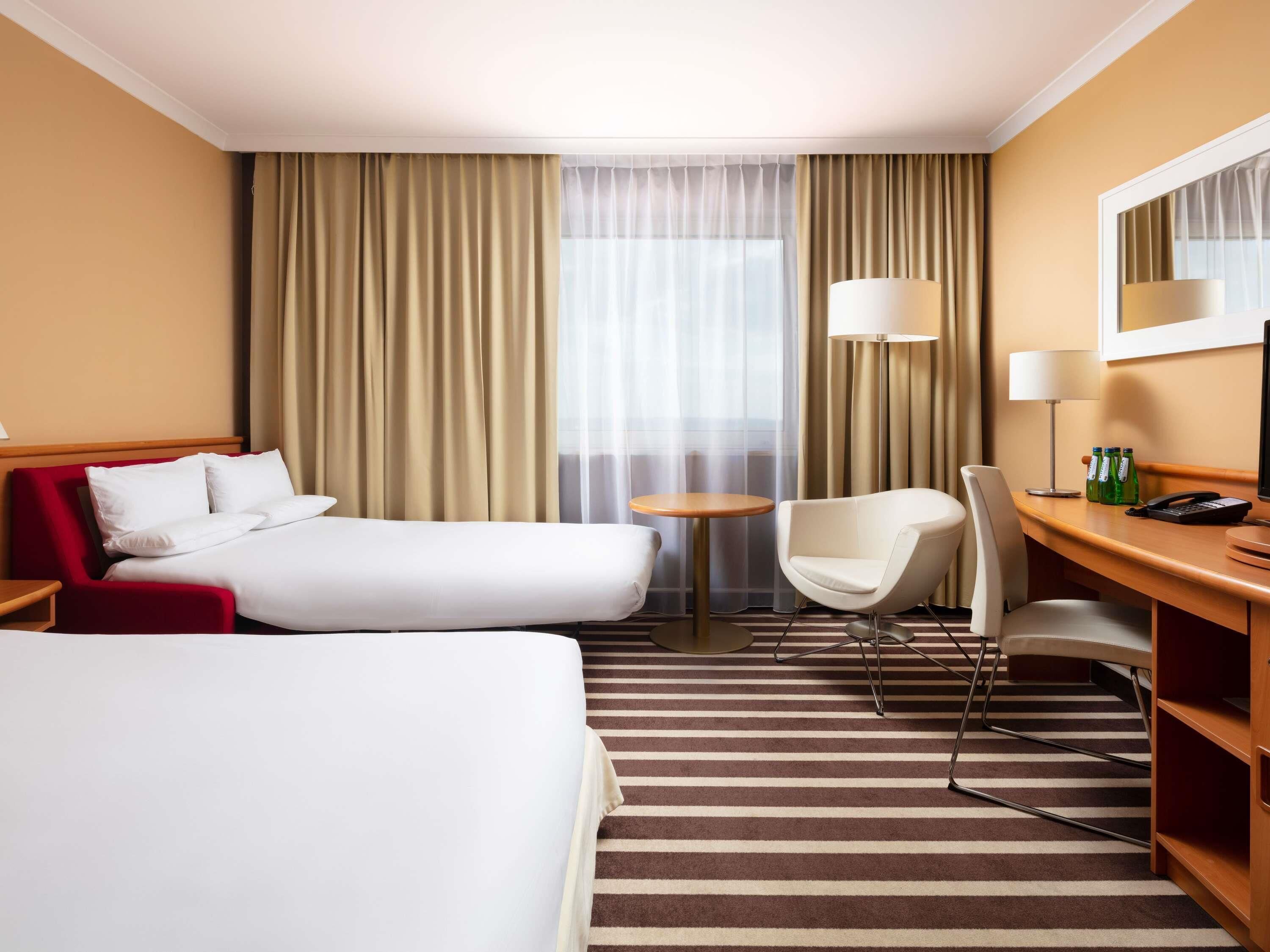 Quarto de hotel com duas camas, uma mesa, uma cadeira, um abajur e um telefone.