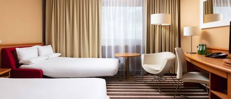 Quarto de hotel com duas camas, uma mesa, uma cadeira, um abajur e um telefone.