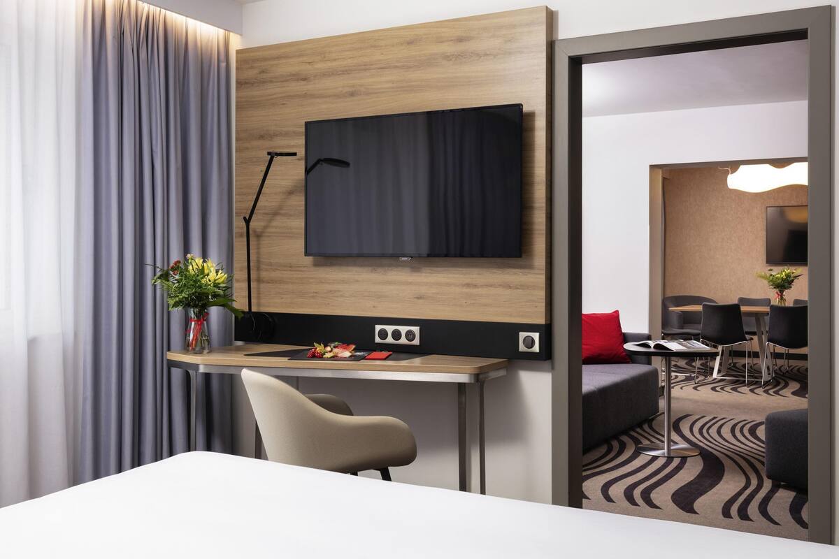Ein modernes Hotelzimmer mit Schreibtisch, Stuhl, Flachbildfernseher und einer Essecke mit Sofa und Sesseln.
