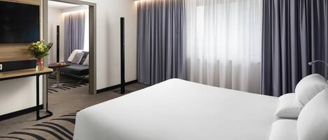 Een moderne hotelkamer met een groot bed, een bureau met stoel, een flatscreen televisie en een groot raam met gordijnen.