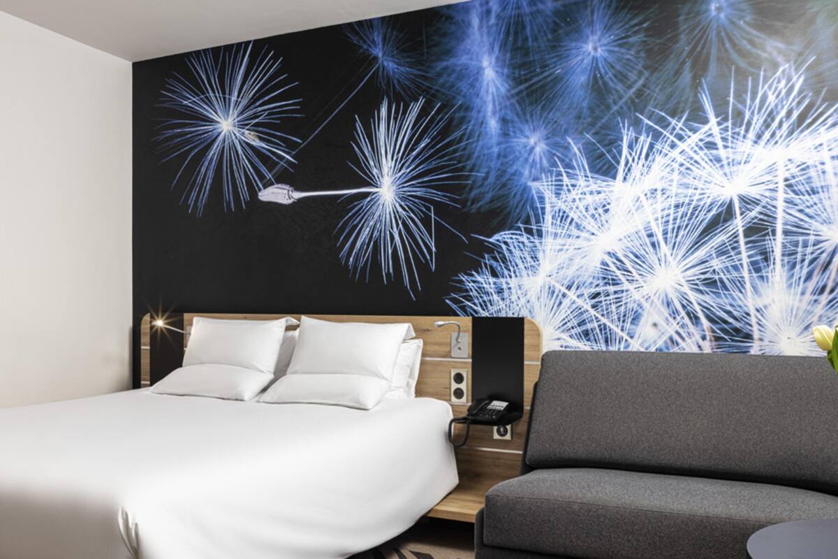 Ein modernes Hotelzimmer mit einem Bett, einem grauen Sofa und einem Wandbild mit Feuerwerk.