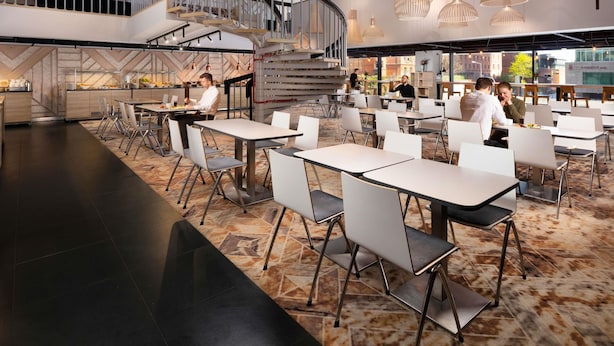 A modern restaurant with a central staircase, dining tables, and chairs.