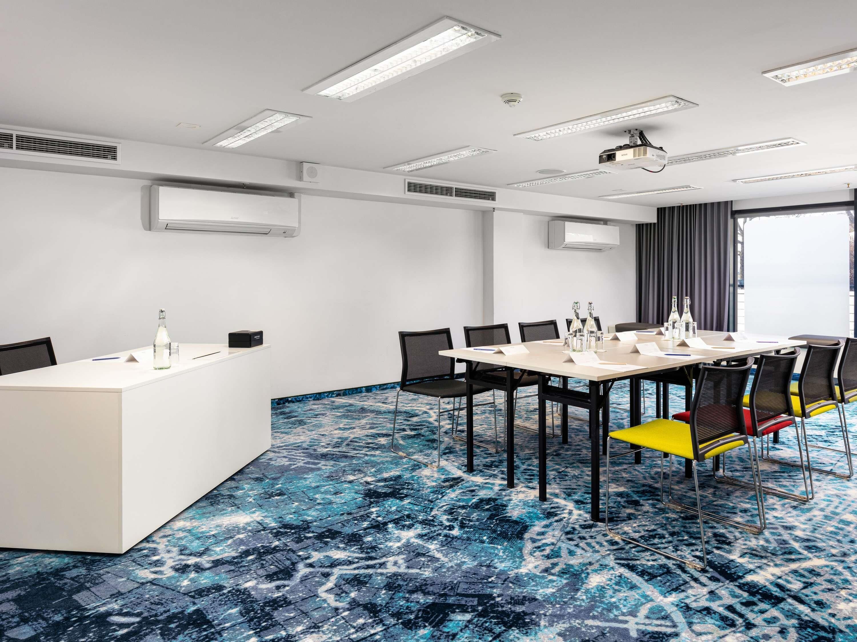 Una sala de conferencias con una mesa blanca, sillas negras y una alfombra azul estampada.