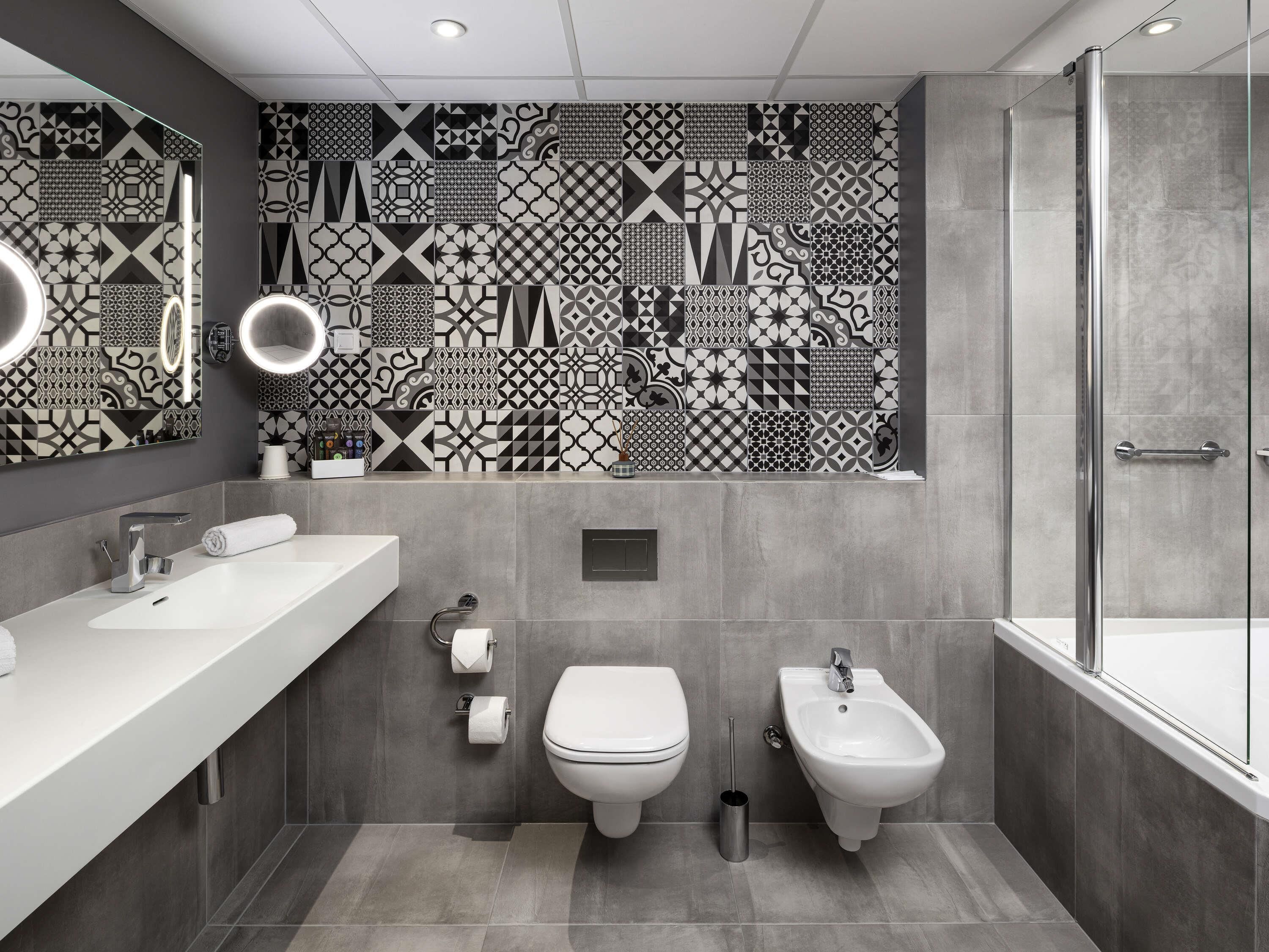 Un baño moderno con salpicadero de azulejos, un tocador con espejo, inodoro, bidé y zona de ducha.