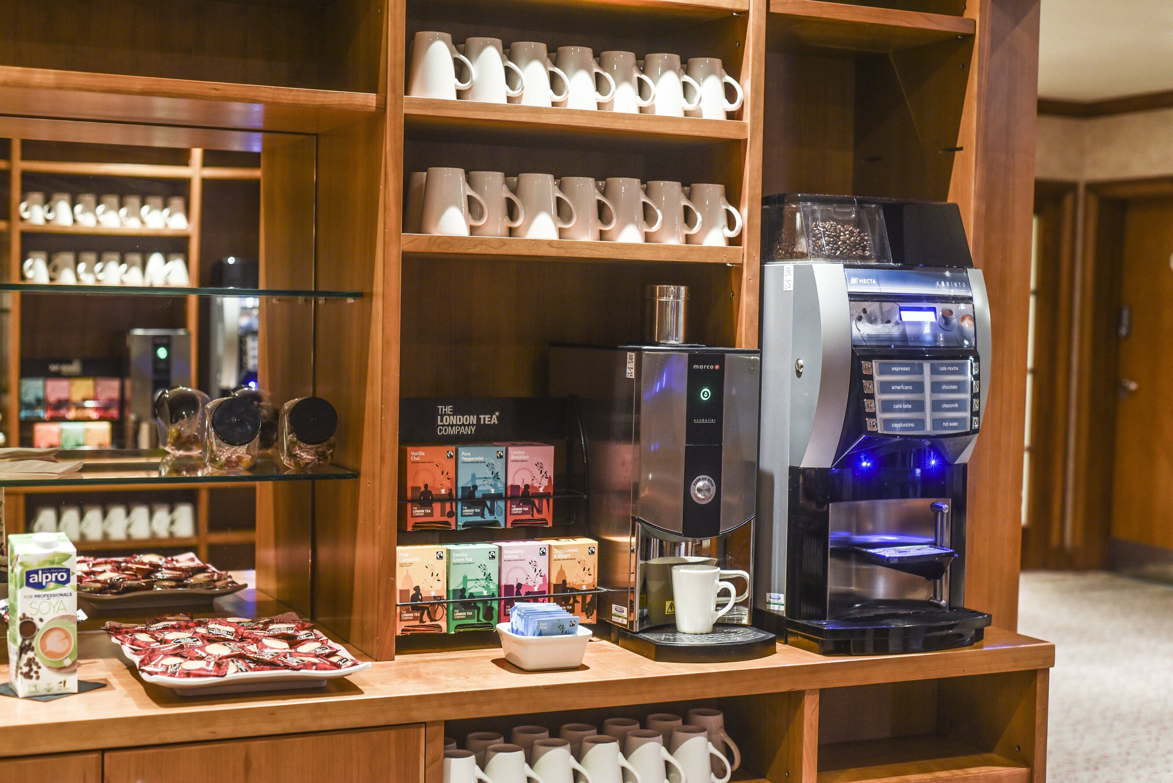 A coffee station with a coffee machine, tea boxes, and a variety of mugs and cups.