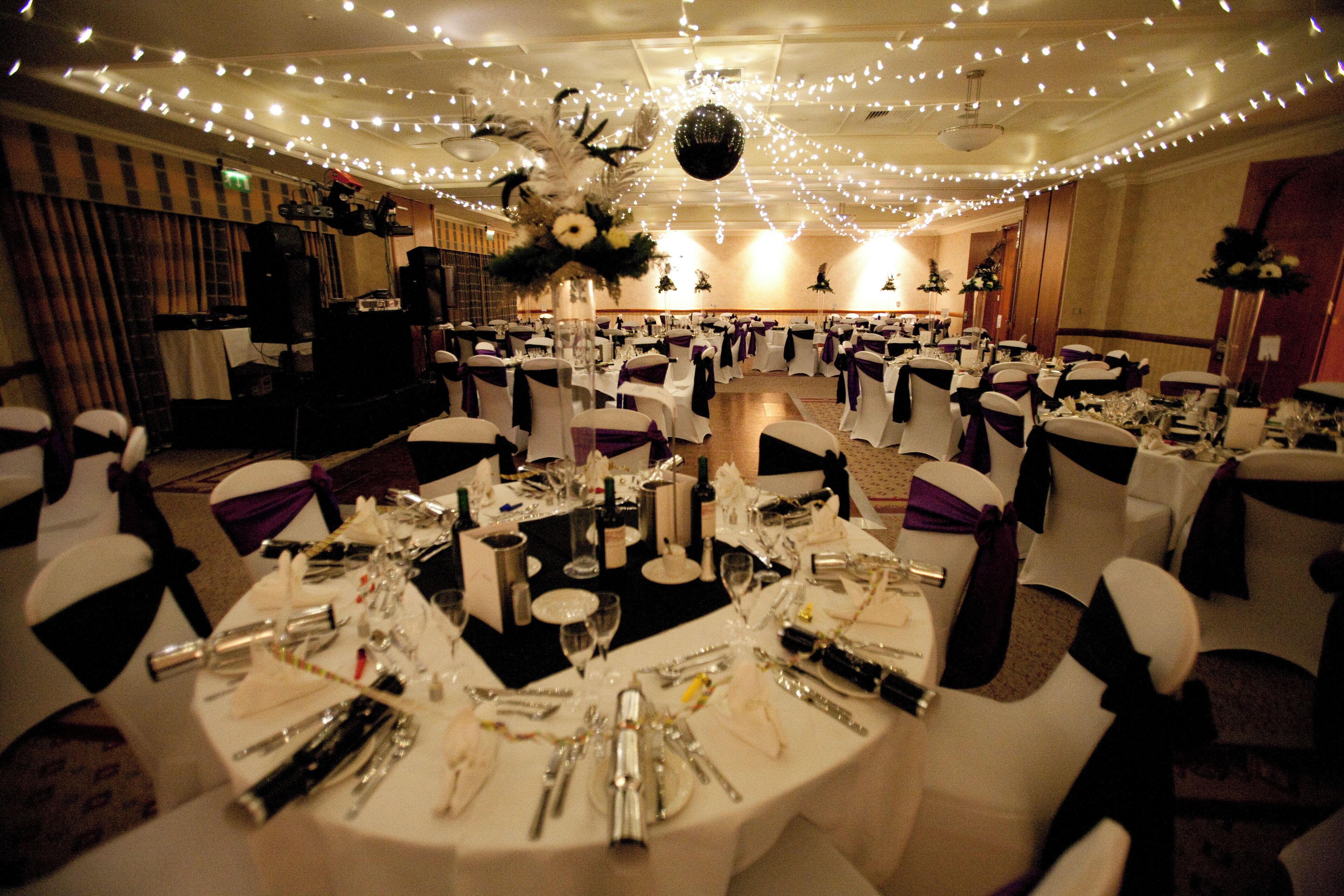Un salón de banquetes con mesas redondas dispuestas para un evento formal, destacando manteles blancos, cubertería y cristalería.