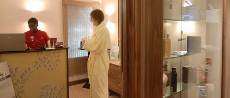A hotel reception area with a receptionist, a reception desk, and a glass display case with toiletries.