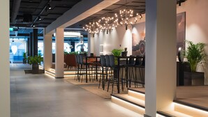 Un interior moderno con un largo pasillo, un área de descanso con mesas y sillas, e iluminación decorativa.