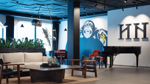 Un área de estar moderna con sofá, mesa de centro, sillas, un piano y un mural en la pared.
