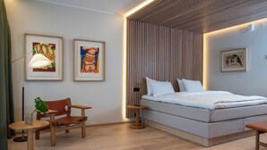 Un dormitorio moderno con cama, una silla, una mesita y obras de arte en las paredes.