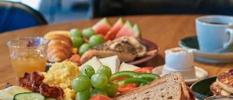Prato de pequeno-almoço com várias comidas, um copo de sumo de laranja e uma chávena de café sobre uma mesa de madeira.