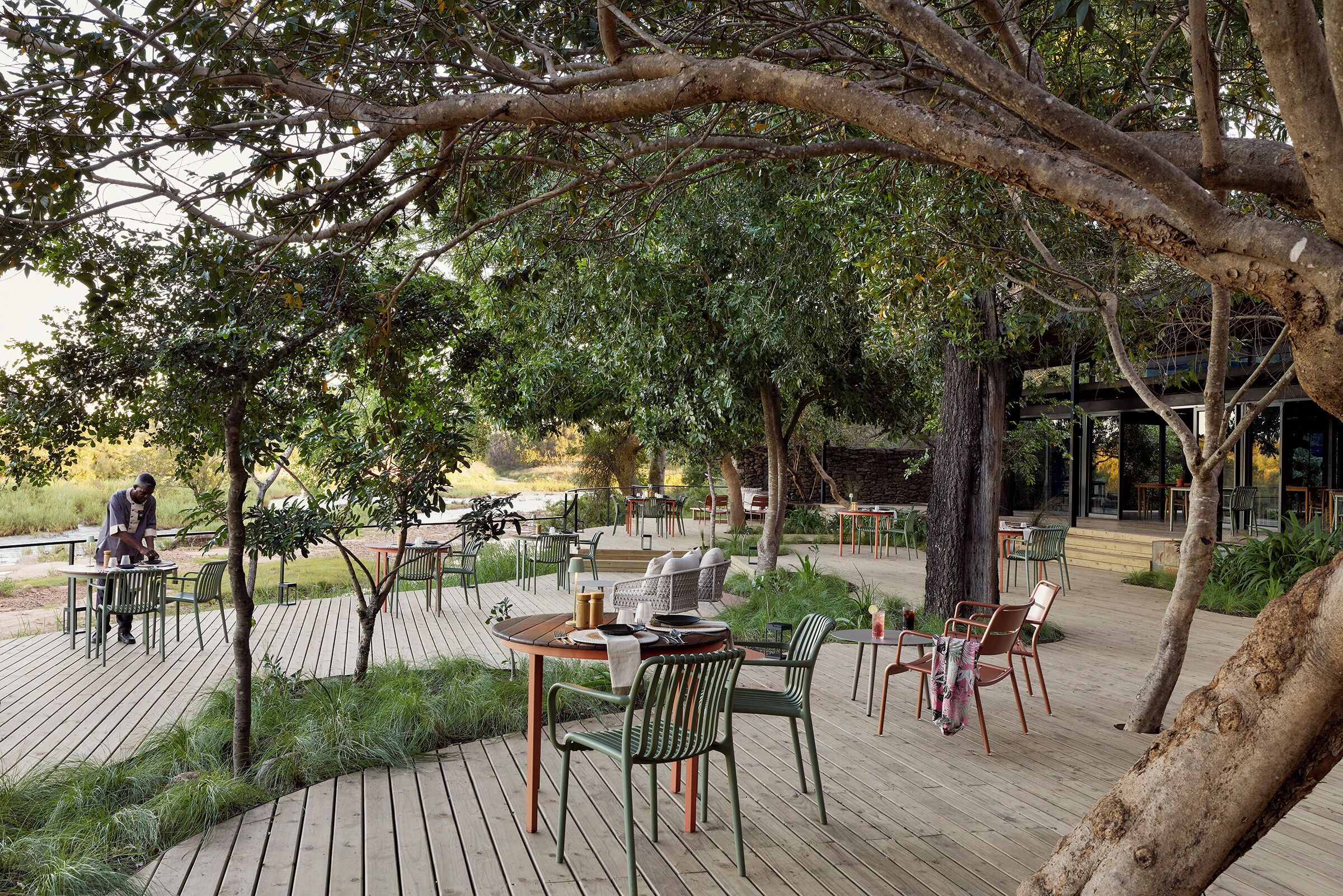 Un espacio de comedor al aire libre con mesas y sillas de madera, rodeado de follaje y árboles.