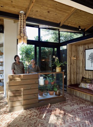 A reception area with a wooden desk, a glass display case with plants, a bench, and a large window with a view of greenery.