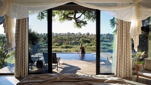 A bedroom with a large bed, a view of a pool, and a deck area with outdoor furniture.