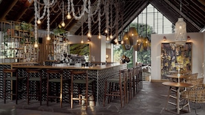 A bar area with a high ceiling, hanging light fixtures, and a view of the outdoors through large windows.