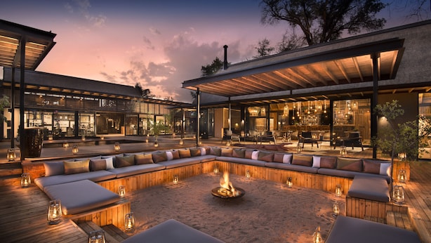 A modern outdoor seating area with a fire pit, wooden deck, and glass-enclosed dining space.
