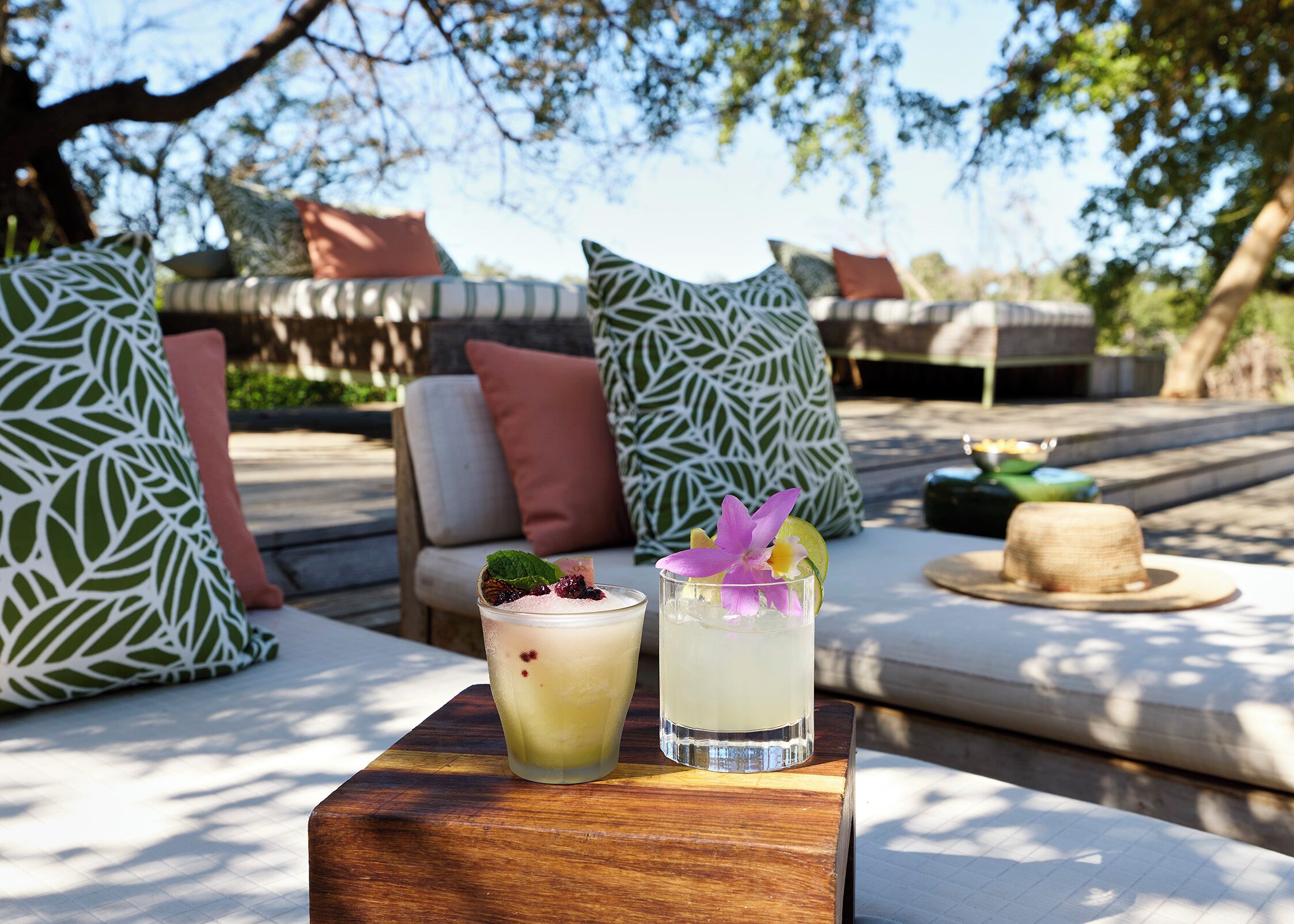 Une table avec deux boissons, un chapeau et un coussin orné d’un motif de feuilles.