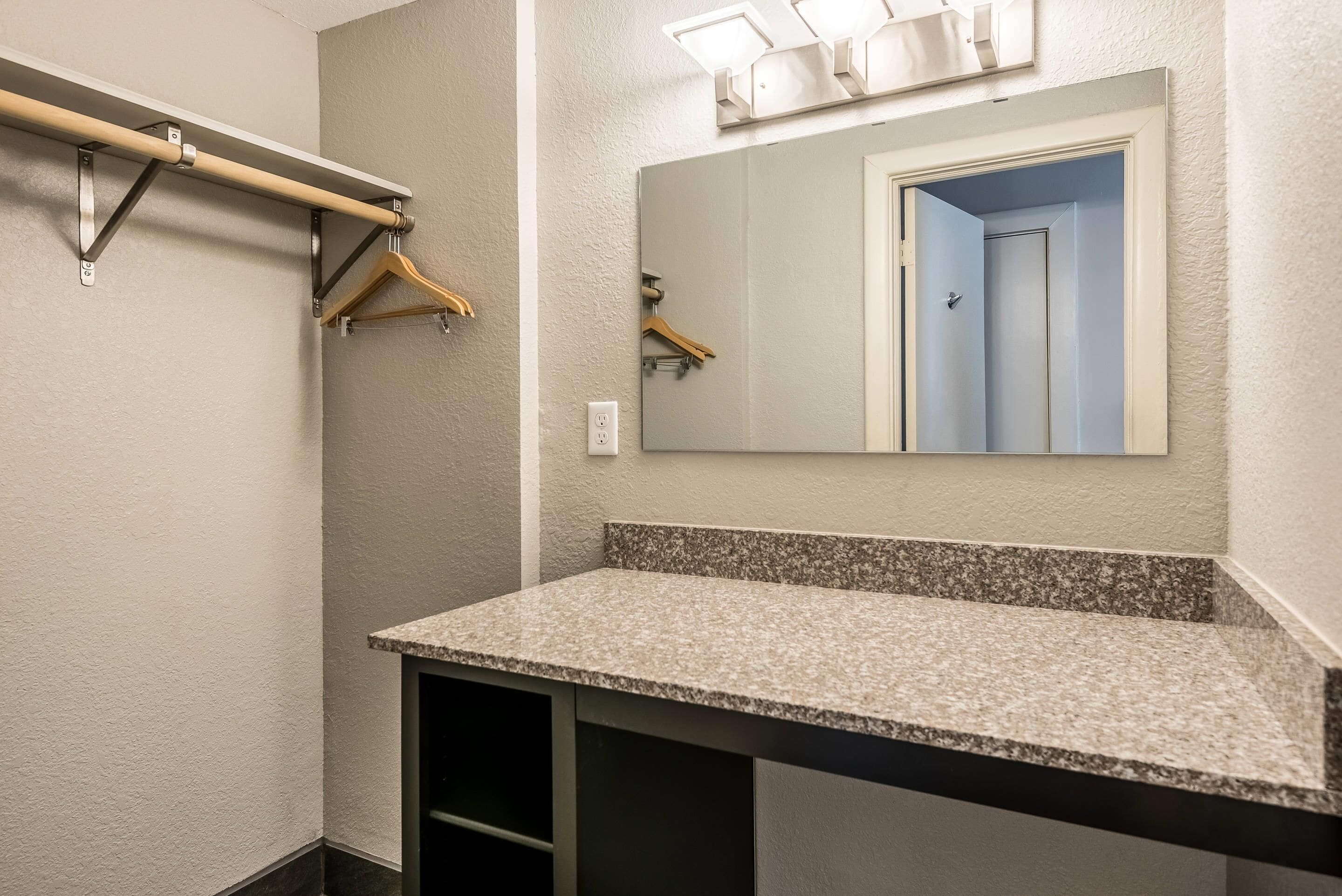 A bathroom with a granite countertop, a towel rack, a mirror, and a door leading to another room.