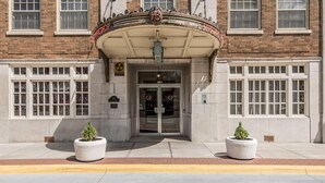 A building entrance with a classic architectural design, featuring a large arched entrance and two potted plants on either side.