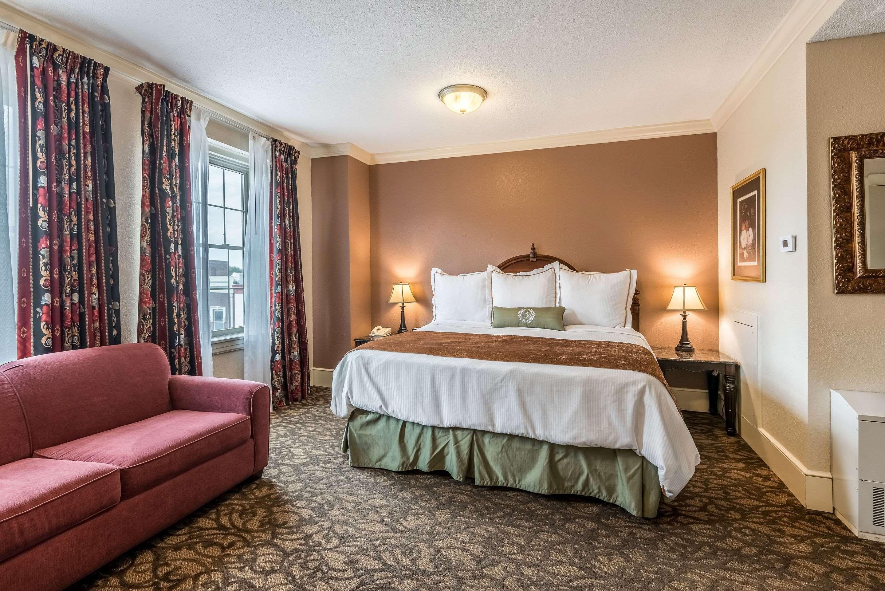 A hotel room with a large bed, two bedside lamps, a red sofa, and patterned carpet.