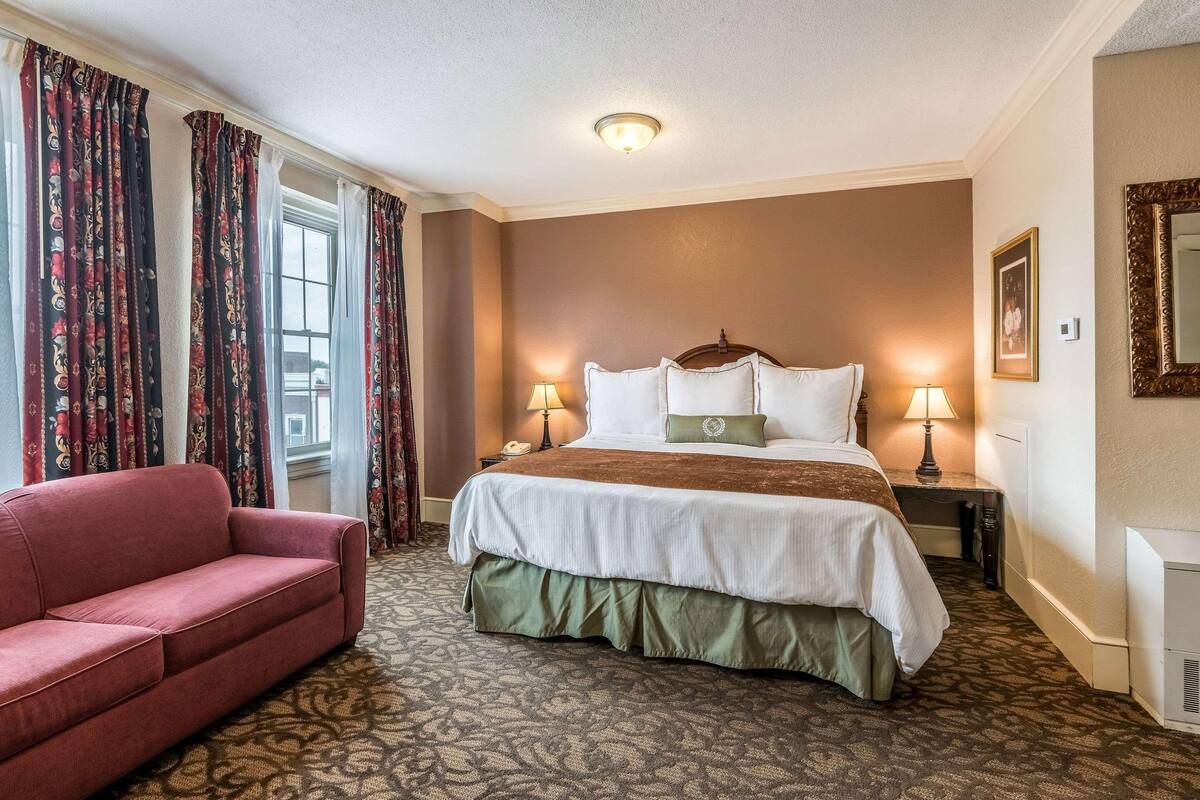 A hotel room with a large bed, two bedside lamps, a red sofa, and patterned carpet.