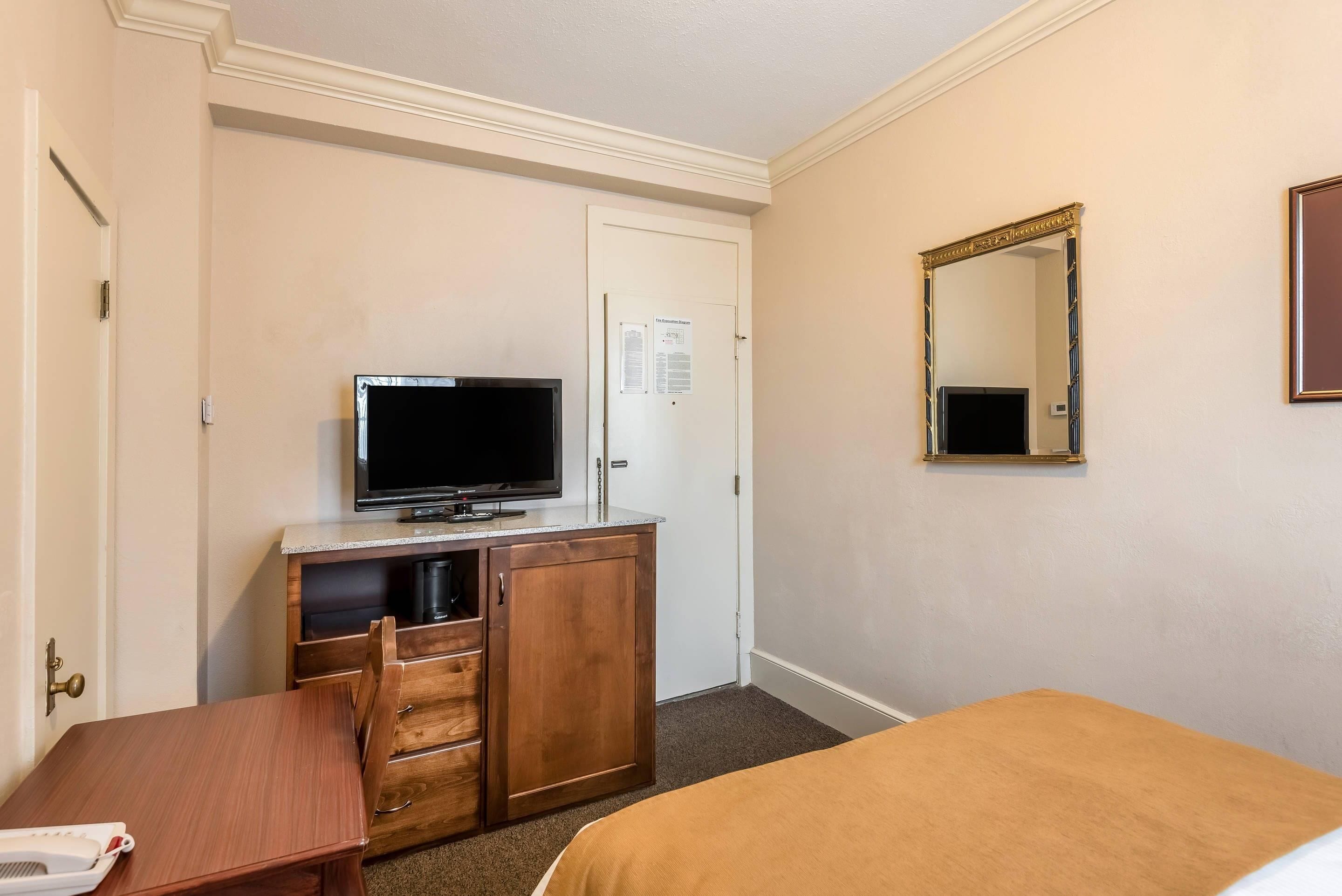 A hotel room with a bed, a desk, a television, a dresser, and a mirror.