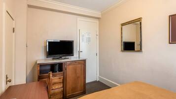 A hotel room with a bed, a desk, a television, a dresser, and a mirror.