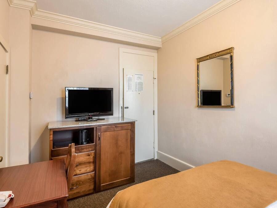 A hotel room with a bed, a desk, a television, a dresser, and a mirror.