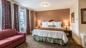 Une chambre d’hôtel avec un grand lit, un canapé rouge, une moquette à motifs et une fenêtre avec des rideaux.