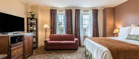 A hotel room with a large bed, a sofa, a TV, and a desk with drawers.