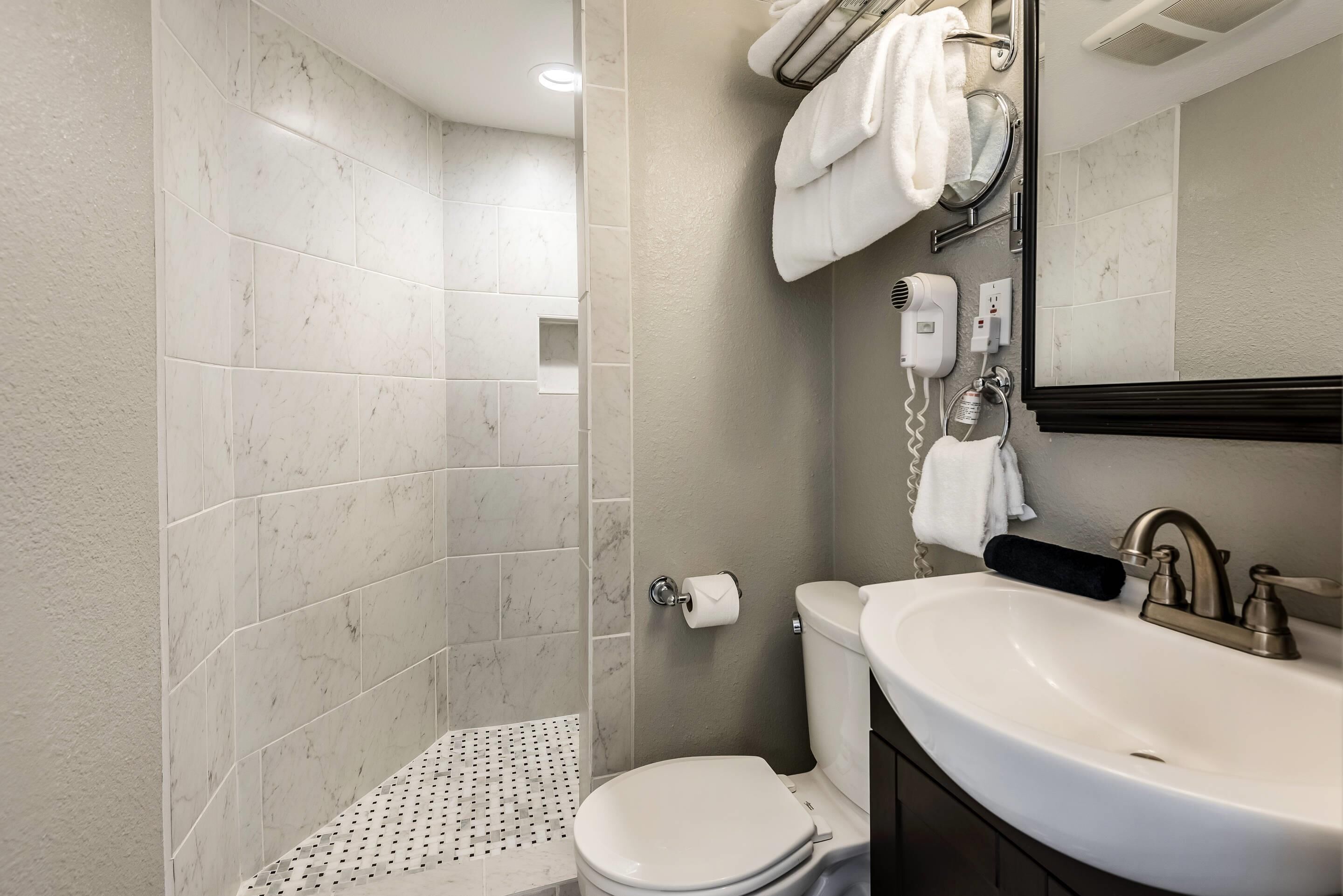 A bathroom with a white toilet, a sink with a mirror, and a shower area with tiled walls.