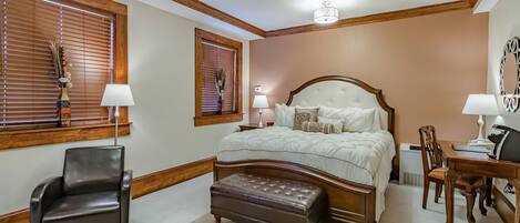 A bedroom with a large bed, wooden headboard, two bedside tables with lamps, a chair, a desk, and a decorative mirror.