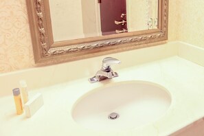 A bathroom with a white sink, a mirror with an ornate frame, and toiletries on the counter.