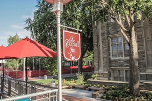 A sign for The Conwell Inn, a stone building with a large tree and red umbrellas in the background.