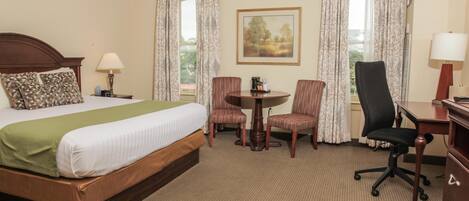 A hotel room with a bed, a desk, two chairs, a table, and a painting on the wall.