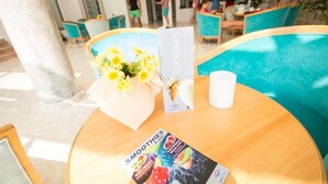 A table with a menu for cocktails and smoothies, a vase with yellow flowers, and a white cup. - Hotel Amic Gala (Palma de Mallorca)