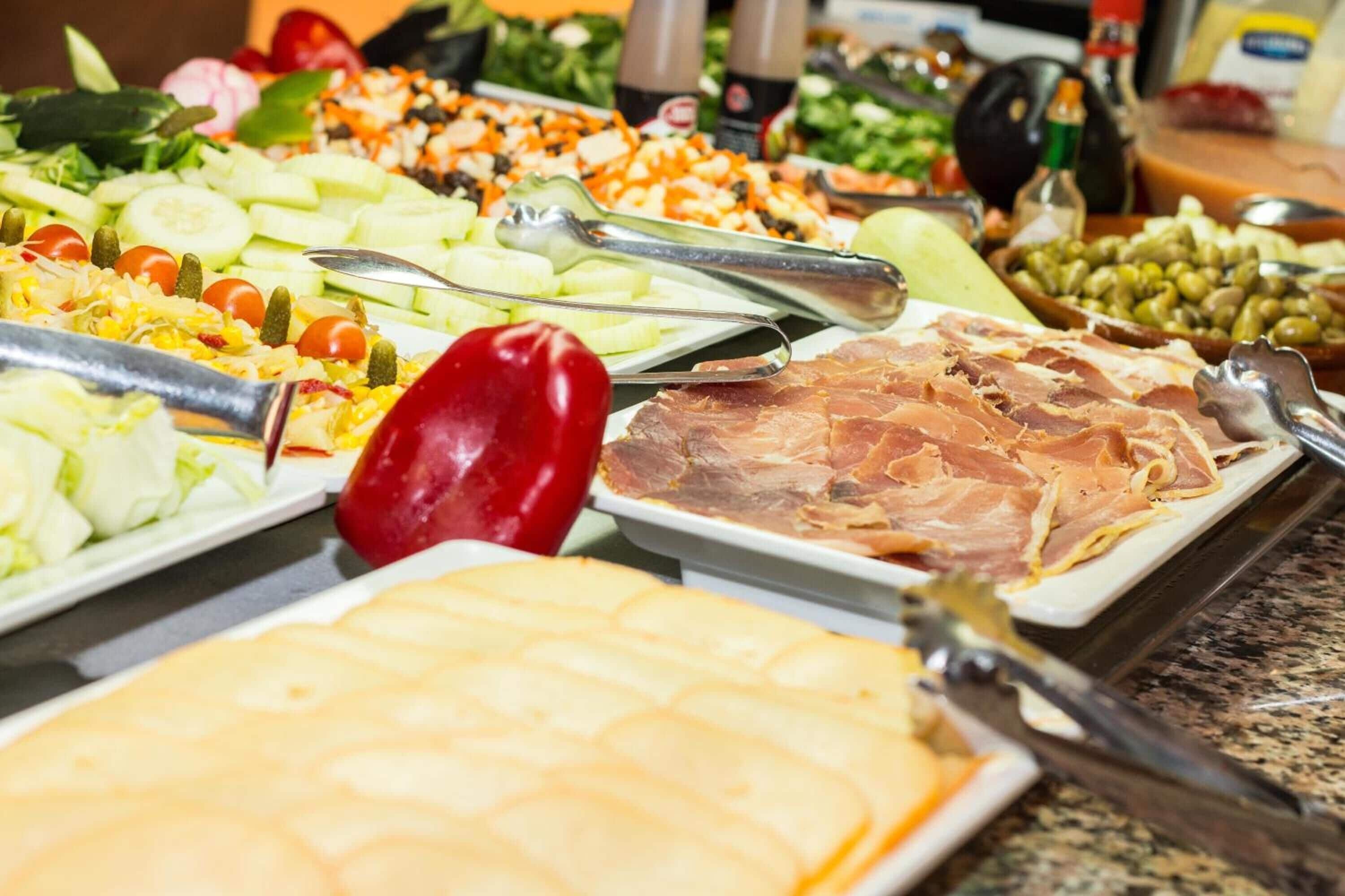 Een buffet met diverse gerechten, waaronder vleeswaren, kazen en groenten.