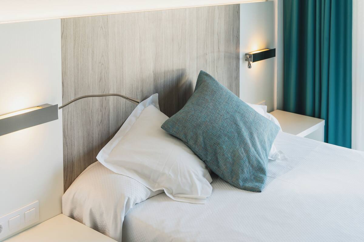 A neatly made bed with white bedding and two pillows, a wooden headboard, and bedside tables with wall-mounted lamps.