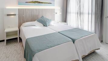 Habitación de hotel con dos camas, una mesita de noche, aire acondicionado de pared y un cuadro con un paisaje costero.