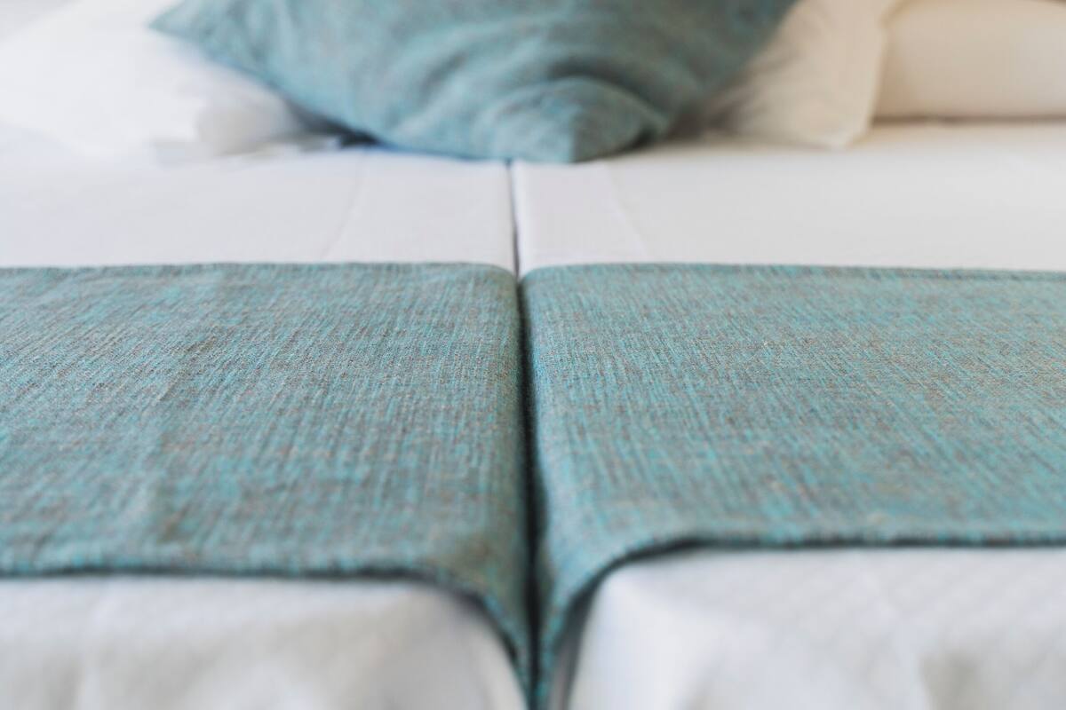 A bed with a teal throw blanket and pillows, a wooden headboard, and a view of a body of water.