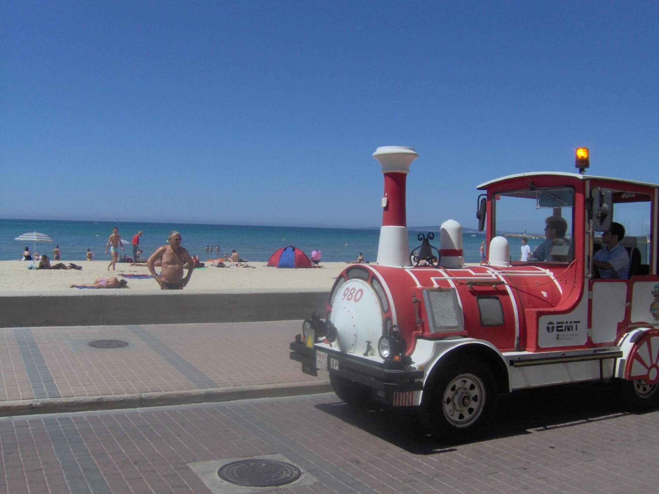 Un tren antiguo rojo y blanco en un paseo marítimo.