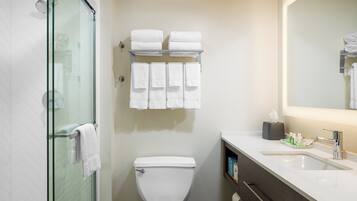 Un baño con cabina de ducha de vidrio, inodoro, lavabo con espejo y toallero con varias toallas.