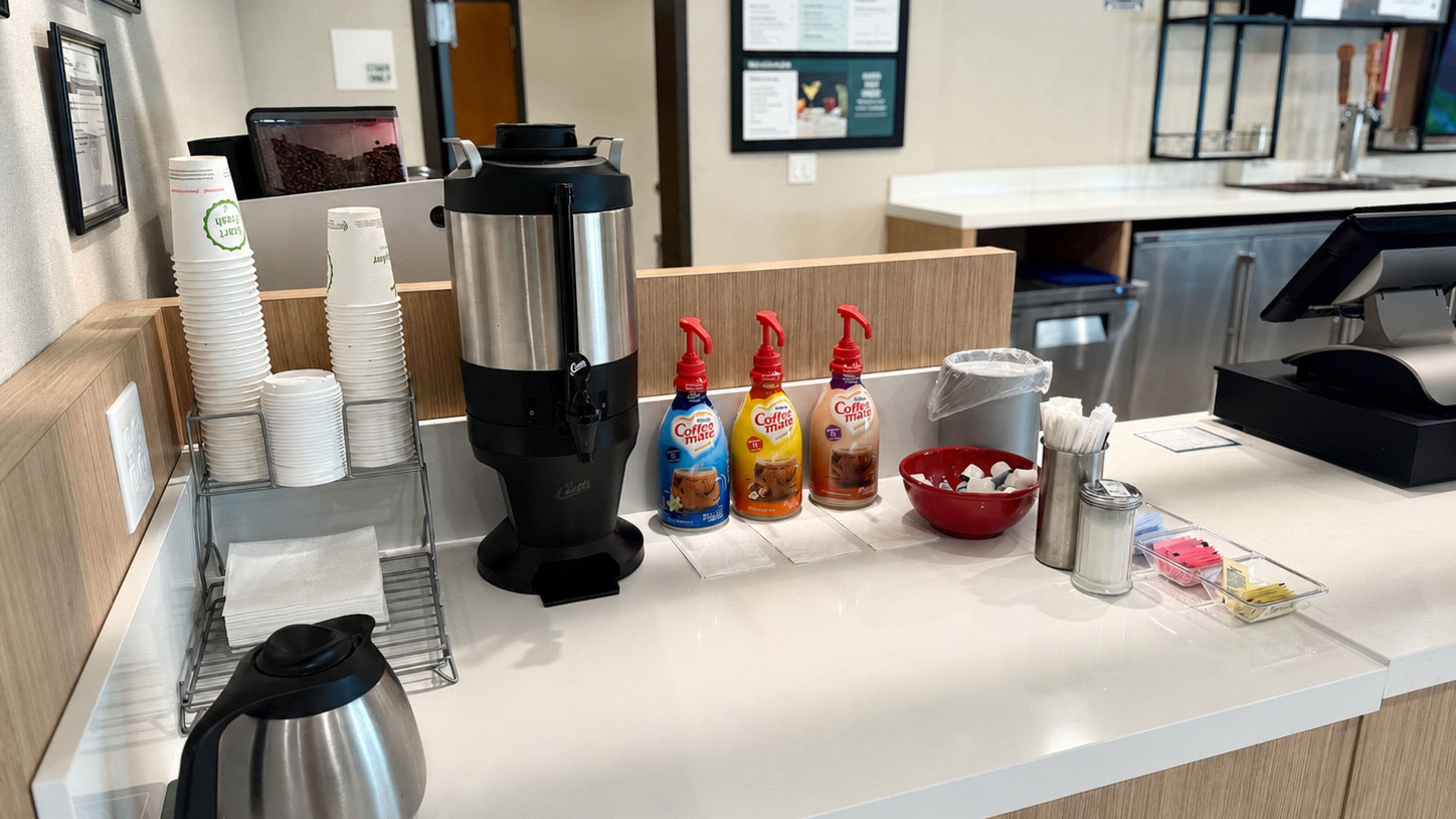 A coffee station with a coffee maker, disposable cups, and coffee drink options.