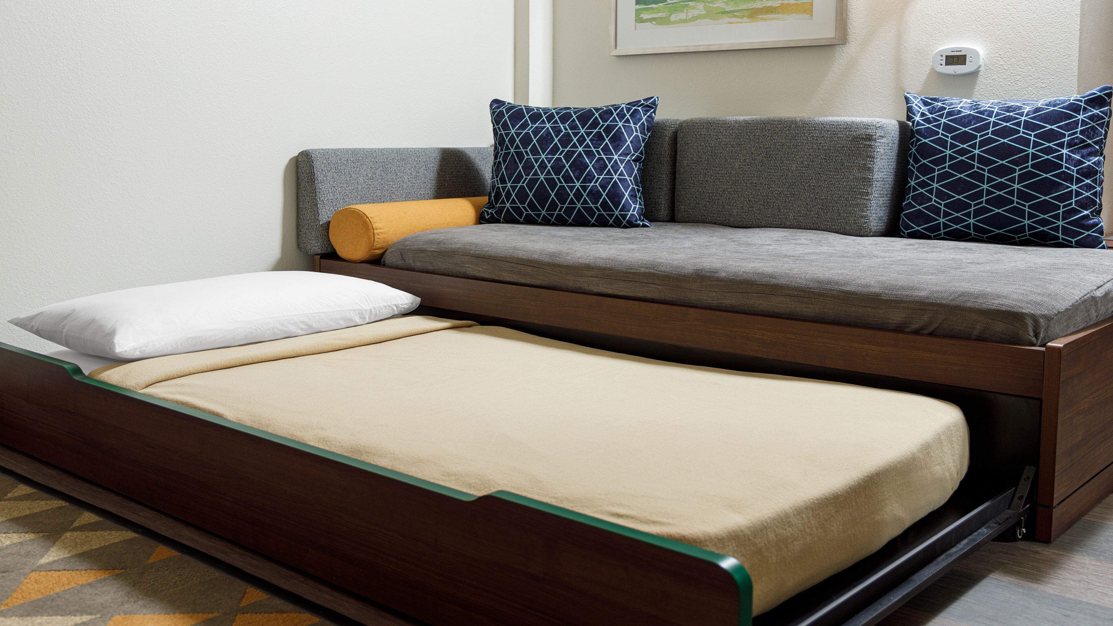 A convertible sofa-bed with a wooden frame, a mattress, and multiple pillows.