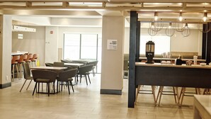 A modern restaurant with a bar area, seating arrangements, and a sign indicating hours of operation. - Holiday Inn Cleveland by IHG (Cleveland)