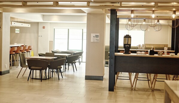 A modern restaurant with a bar area, seating arrangements, and a sign indicating hours of operation. - Holiday Inn Cleveland by IHG (Cleveland)