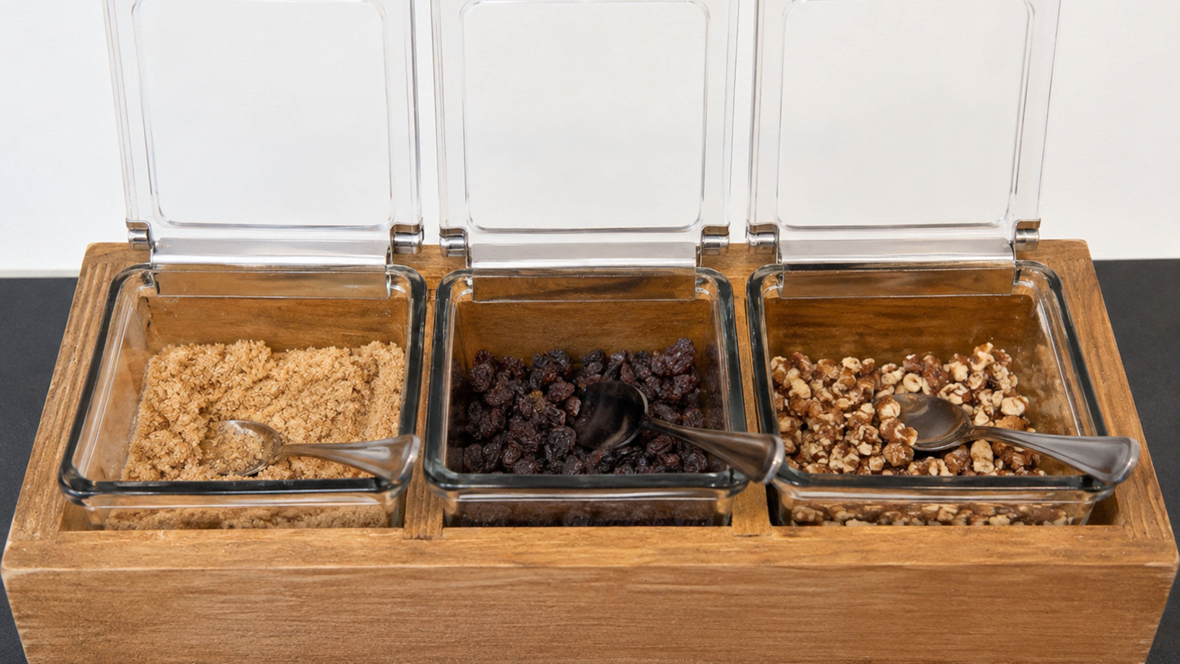 A wooden container with three glass compartments, each containing different food items and a spoon.